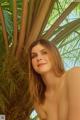 A woman in a bikini posing in front of a palm tree.