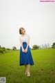 A woman in a white shirt and blue skirt standing in a field.