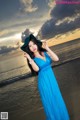 A woman in a blue dress and hat standing on the beach.