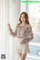 A woman standing in front of a window wearing a floral blouse.