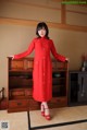 A woman in a red dress standing in front of a dresser.