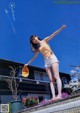 A woman standing on the edge of a swimming pool holding a hat.