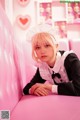 A woman in a maid outfit sitting on a pink couch.