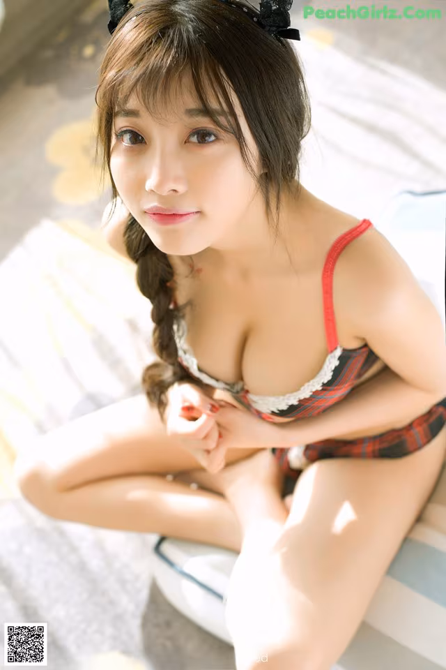 A woman in a red and black lingerie sitting on a bed.