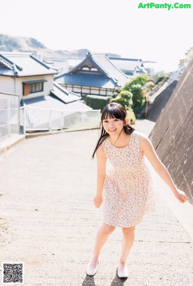 A young girl in a floral dress is walking down a path.