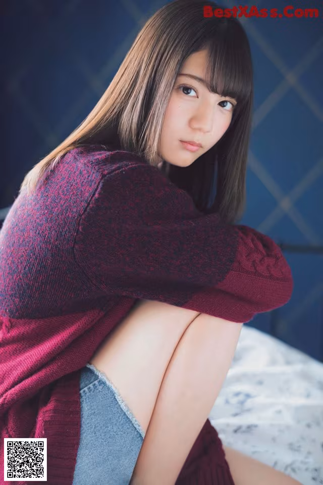A woman sitting on top of a bed wearing a red sweater.