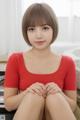 A woman in a red shirt sitting on a bed.