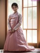 A woman in a pink hanbok standing in front of a window.