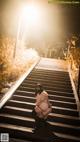 A woman crouching down on a set of stairs at night.