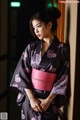 A woman in a black and pink kimono leaning against a wall.